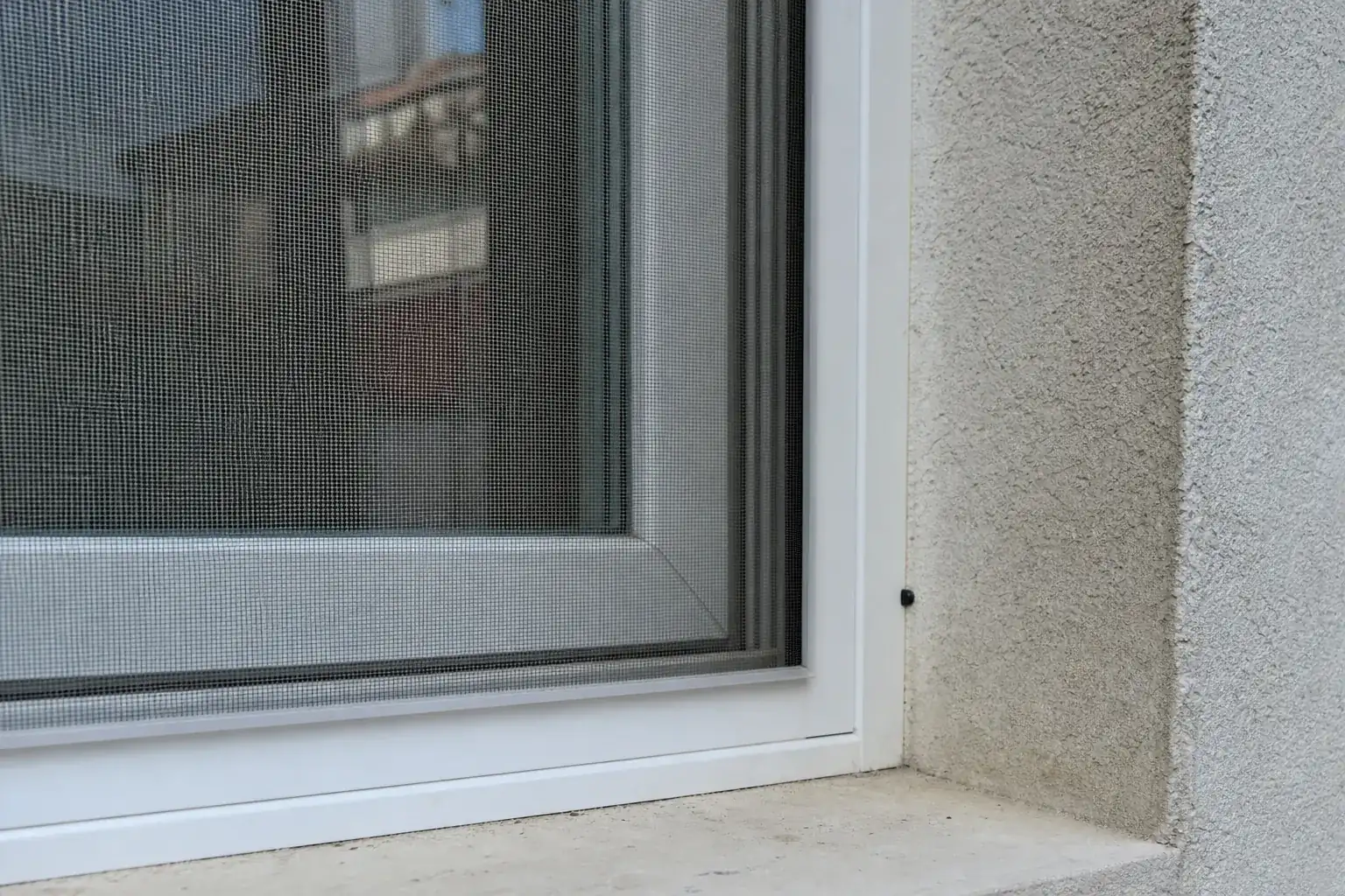 Moustiquaire à cadre fixe posée sur une fenêtre battante, vue rapprochée du cadre