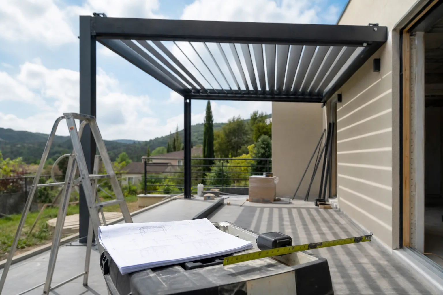 Pergola bioclimatique en cours d’installation sur une terrasse, mètre ruban et notice de pose