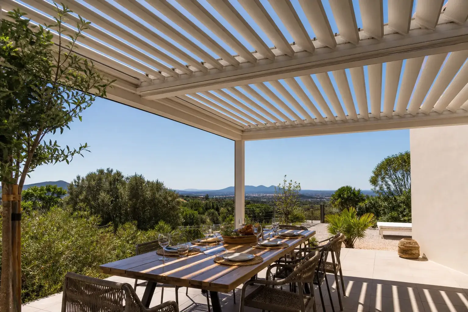 Terrasse méditerranéenne habitée sous une pergola bioclimatique, lames orientables mi-ouvertes