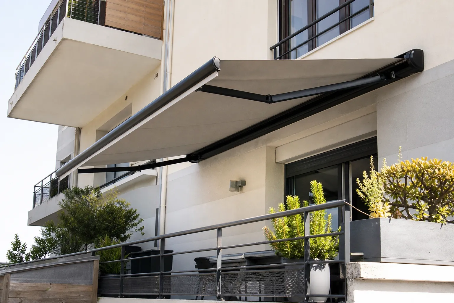 Store banne à bras articulés déployé au-dessus d’une terrasse, toile unie